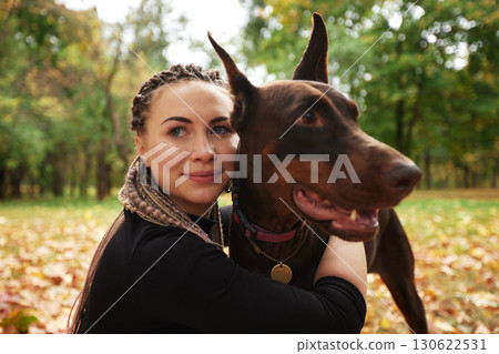 Woman Embracing a Brown Doberman Dog in an Autumn Park Setting 130622531