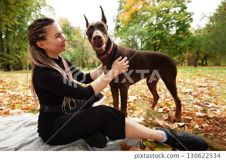 Woman with braided hair spending quality time with her Doberman in autumn park 130622534