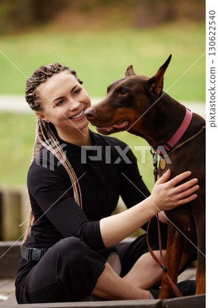 Woman enjoys bonding time with her Doberman in a park setting Woman enjoys bonding time with her Doberman in a park setting 130622540
