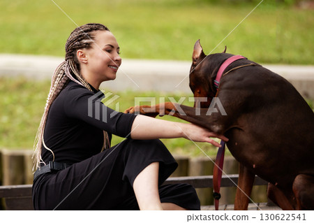 Woman smiling while bonding with her playful Doberman outdoors Woman smiling while bonding with her playful Doberman outdoors 130622541