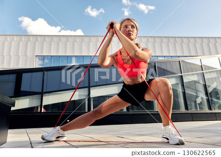 Woman Performing Fitness Exercises Outdoors Using Resistance Bands 130622565