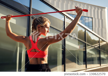 Athletic woman exercising outdoors with resistance band under bright sunlight 130622570