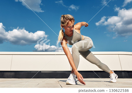 Woman performing fitness stretches outdoors under a sunny sky 130622586