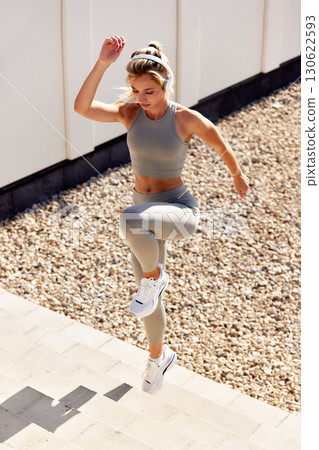 Woman exercising outdoors in sportswear, performing stairs workout under sunlight Woman exercising outdoors in sportswear, performing stairs workout under sunlight 130622593