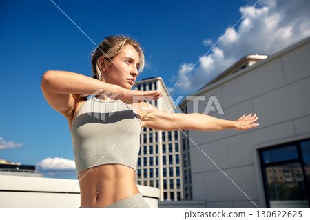 Fit woman practicing exercise in urban rooftop with blue skies and clouds 130622625