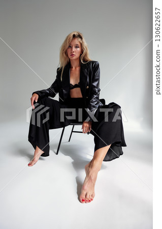 Fashionable woman in black outfit sitting confidently in contemporary studio setting 130622657