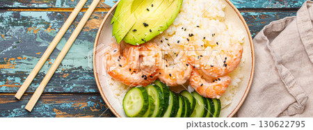 White ceramic bowl with rice, shrimps, avocado, vegetables and sesame seeds and chopsticks on colourful rustic wooden background top view. Healthy asian style poke bowl White ceramic bowl with rice, shrimps, avocado, vegetables and sesame seeds and chopsticks on colourful rustic wooden background top view. Healthy asian style poke bowl 130622795