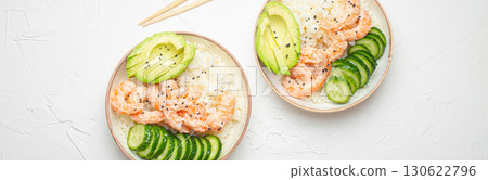 Two white ceramic bowls with rice, shrimps, avocado, vegetables and sesame seeds and wooden sticks on white concrete stone background top view. Healthy asian style poke bowl Two white ceramic bowls with rice, shrimps, avocado, vegetables and sesame seeds and wooden sticks on white concrete stone background top view. Healthy asian style poke bowl 130622796