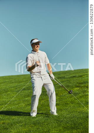 Smiling golfer celebrating with raised fist holding club on green course Smiling golfer celebrating with raised fist holding club on green course 130622879