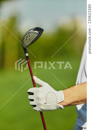 Vertical close up of golfer hand in glove holding club against blurred green background 130622880