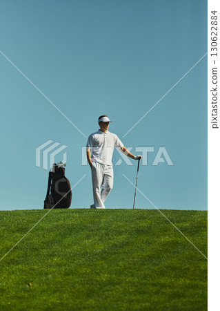 Golfer standing with club and bag on sunny course 130622884