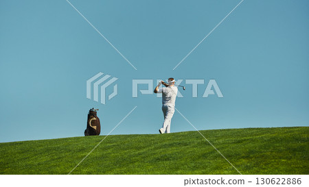 Golfer swinging club on green fairway under clear sky 130622886