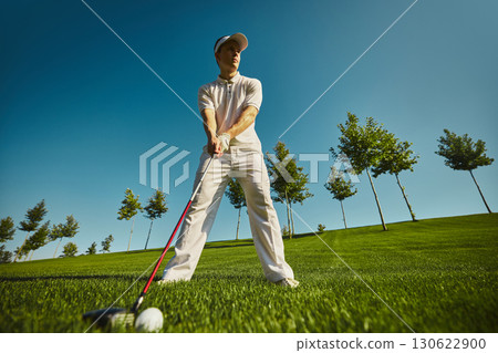 Golfer preparing shot with ball on grass under blue sky Golfer preparing shot with ball on grass under blue sky 130622900