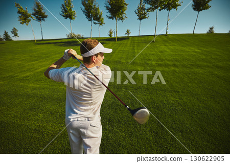 Golfer swinging club on sunny green course with trees Golfer swinging club on sunny green course with trees 130622905