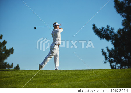 Golfer completing dynamic swing on sunny golf course Golfer completing dynamic swing on sunny golf course 130622914