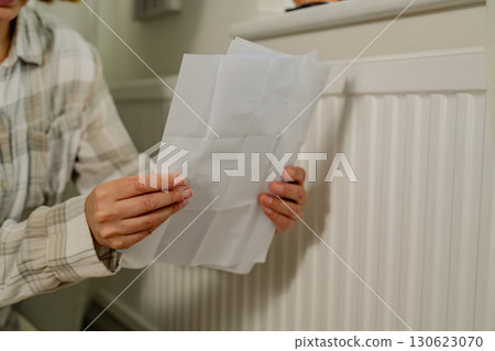Woman holding utility paper bills next to heating thermostat, increasing heating costs 130623070