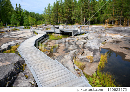Wooden boardwalk amidst rocky terrain in forest, area of prehistoric petroglyphs with stone and water in Zalavruga, Karelia Wooden boardwalk amidst rocky terrain in forest, area of prehistoric petroglyphs with stone and water in Zalavruga, Karelia 130623373