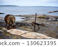 Weathered anchor and old rusty winch on rocky coastal shoreline by White Sea in Karelia, rustic landscape, nature of Russia 130623395