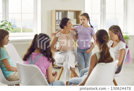 School psychologist woman having conversation with group of children girls sitting in a circle. 130624478