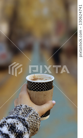 Hand holding takeaway pumpkin spice latte cup in blurred autumn park background with shallow depth of field perfect for lifestyle concept coffee advertising seasonal branding and cozy fall promotion 130624741