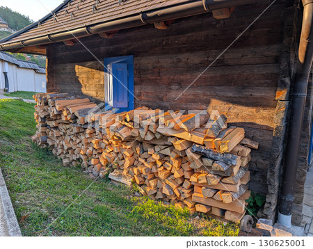 Piles of firewood near wooden house with colorful windows. Village lifestyle and architecture. 130625001