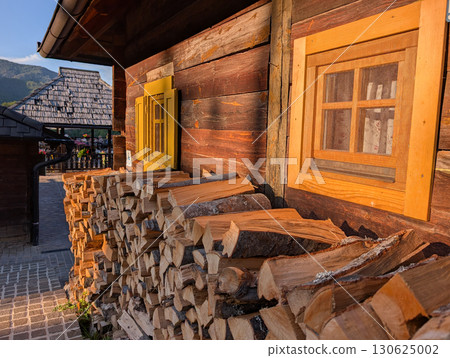 Piles of firewood near wooden house with colorful windows. Village lifestyle and architecture. 130625002