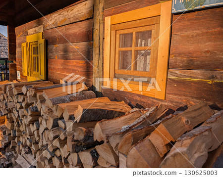 Piles of firewood near wooden house with colorful windows. Village lifestyle and architecture. 130625003