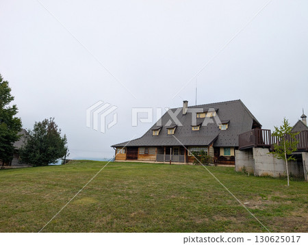 A large wooden house with a steep gray roof and small windows. Rural architecture, countryside lifestyle, and traditional building style in the Serbian mountains. A large wooden house with a steep gray roof and small windows. Rural architecture, countryside lifestyle, and traditional building style in the Serbian mountains. 130625017
