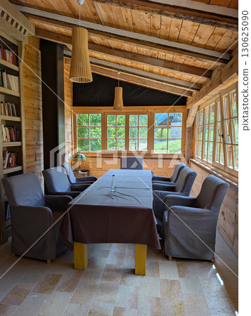 Wooden interior with grey armchairs around a table. Cozy rustic dining space, relaxation, gathering and traditional wooden architecture. 130625090