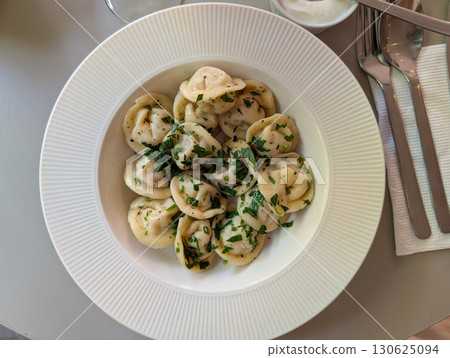 A bowl of dumplings garnished with herbs served with cocktail at cafe table. Culinary tradition, modern dining, and lifestyle gastronomy combining taste and culture. 130625094