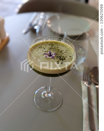 A green cocktail served in a glass with garnish on a cafe table. Culinary art, lifestyle refreshment, and the culture of mixology in a modern dining setting. 130625099