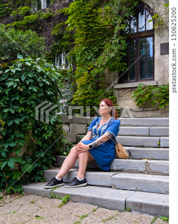 A woman sits relaxed on stone steps surrounded by green ivy walls. Lifestyle fashion, urban culture, and the connection of heritage architecture with modern portraiture. 130625200