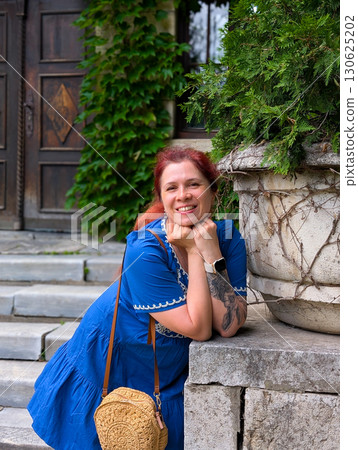 A closeup of a smiling woman leaning near stone steps with greenery. Emotional lifestyle, joyful portrait, and the personal expression of happiness outdoors. 130625202