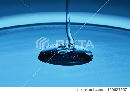 The viscous gel serum for the face flows and collects into a drop on a blue background.. 130625267