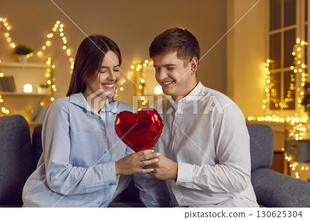 Couple sitting on sofa looking at red heart in bedroom with garlands 130625304