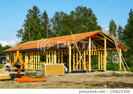 Wooden house frame under construction with roof structure and building materials on site 130625306