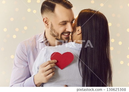 Young happy smiling man holding red paper heart in hand and hugging brunette girl. Young happy smiling man holding red paper heart in hand and hugging brunette girl. 130625308