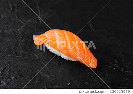 Salmon nigiri resting on dark stone surface Salmon nigiri resting on dark stone surface 130625979