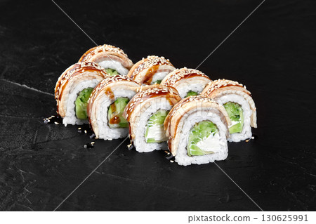 Dragon rolls with eel, avocado, cream cheese and sesame seeds resting on dark stone surface Dragon rolls with eel, avocado, cream cheese and sesame seeds resting on dark stone surface 130625991