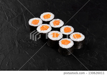 Delicious sushi rolls with salmon and rice filling resting on black stone surface Delicious sushi rolls with salmon and rice filling resting on black stone surface 130626011
