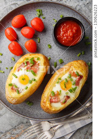 Baked potato in jacket loaded with bacon and egg closeup on the plate on the table. Vertical top view Baked potato in jacket loaded with bacon and egg closeup on the plate on the table. Vertical top view 130626223