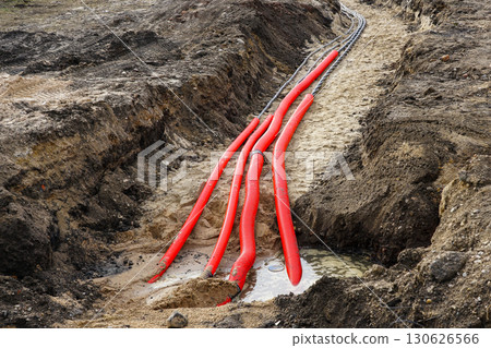 Red Corrugated Conduits and Electrical Cables Laid in Sandy Construction Trench with Standing Water 130626566