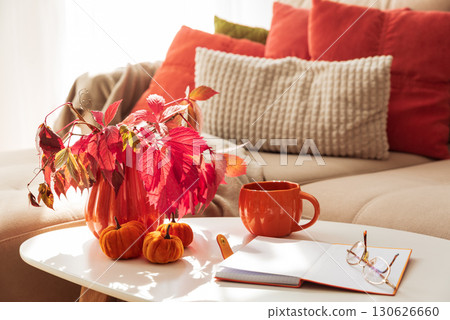Cozy Autumn Living Room Scene with Mug, Notebook and Seasonal Decor under Sun Light 130626660