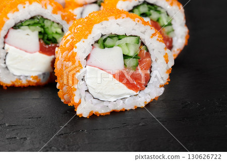 Close-up of tempting california rolls sprinkled with orange tobiko, filled with fresh salmon, cucumber, surimi and cheese, presented on a dark slate plate 130626722