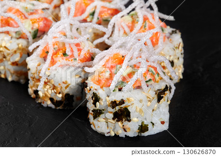 Delicious sushi rolls decorated with crispy rice noodles and salmon on black background Delicious sushi rolls decorated with crispy rice noodles and salmon on black background 130626870
