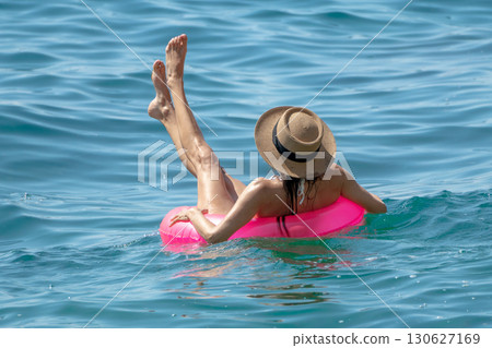 Woman Floating Water, relaxing on pink ring with straw hat, legs up in blue sea for sunny summer vacation. Woman Floating Water, relaxing on pink ring with straw hat, legs up in blue sea for sunny summer vacation. 130627169