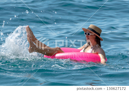 Woman splashing ocean: Relaxed woman on pink float kicking legs, creating water splashes in blue sea for fun. 130627172