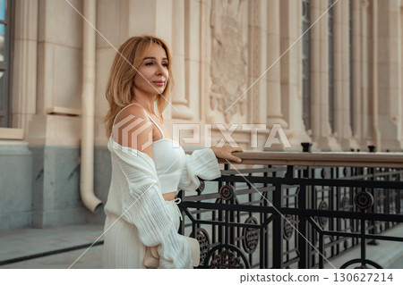 Woman White Outfit Balcony Fashion - A blonde woman wearing a white outfit stands on a balcony, looking to her right. The background is a white building with ornate details. Woman White Outfit Balcony Fashion - A blonde woman wearing a white outfit stands on a balcony, looking to her right. The background is a white building with ornate details. 130627214