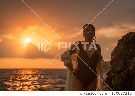 Woman Sunset Beach Rocky Coastline - Enjoying a scenic sunset by the ocean, a woman stands on a rocky coastline. 130627216