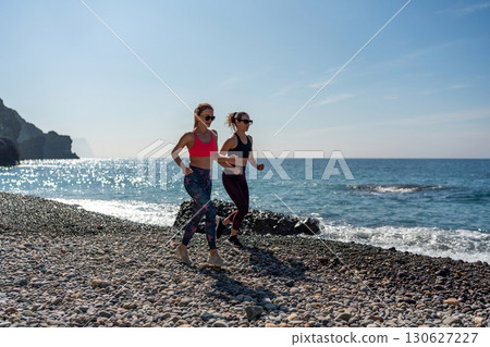 Beach Running Fitness: Two women jog on sunny pebble beach for exercise, daytime cardio workout. 130627227